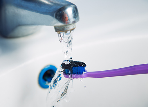 Person rising off toothbrush with black toothpaste in sink