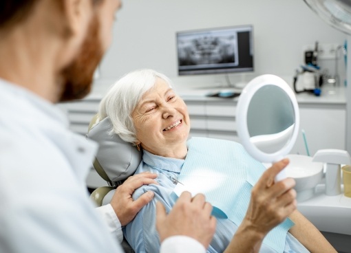 Senior dental patient admiring her smile in mirror