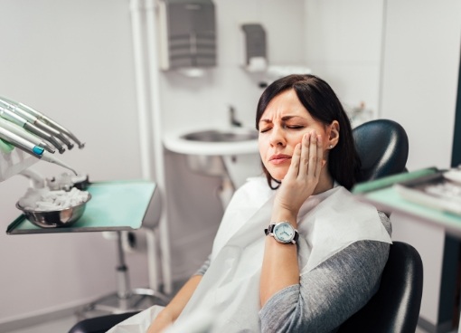 Woman in dental chair touching her face in pain