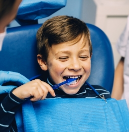 Smiling young boy brushing his teeth in dental chair