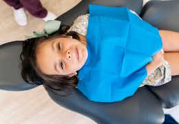 Young girl in dental chair wearing blue dental bib