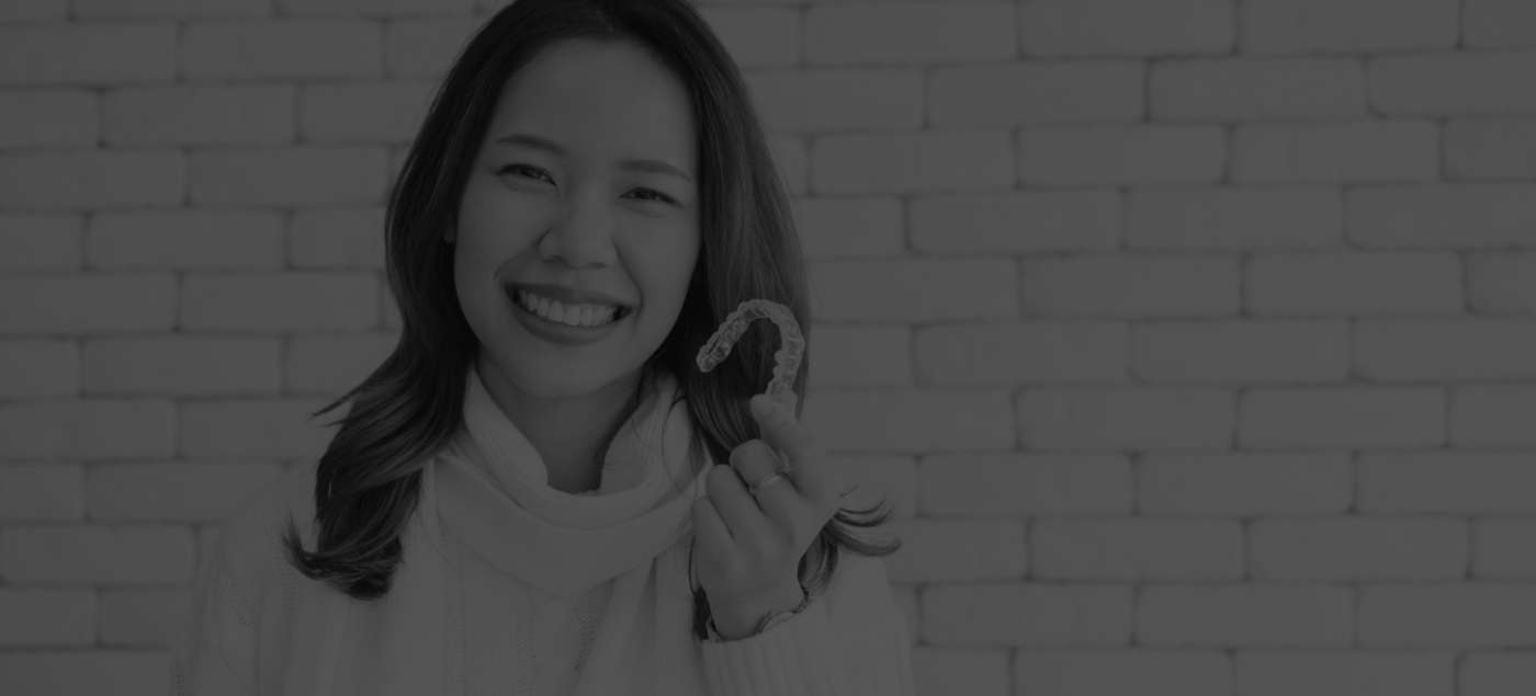 Smiling woman in white sweater holding aligner