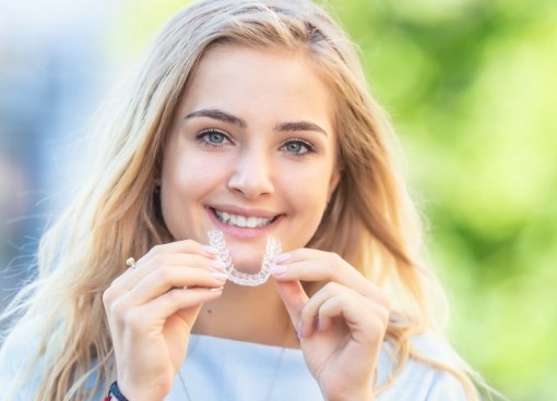 Smiling young woman holding Invisalign outdoors